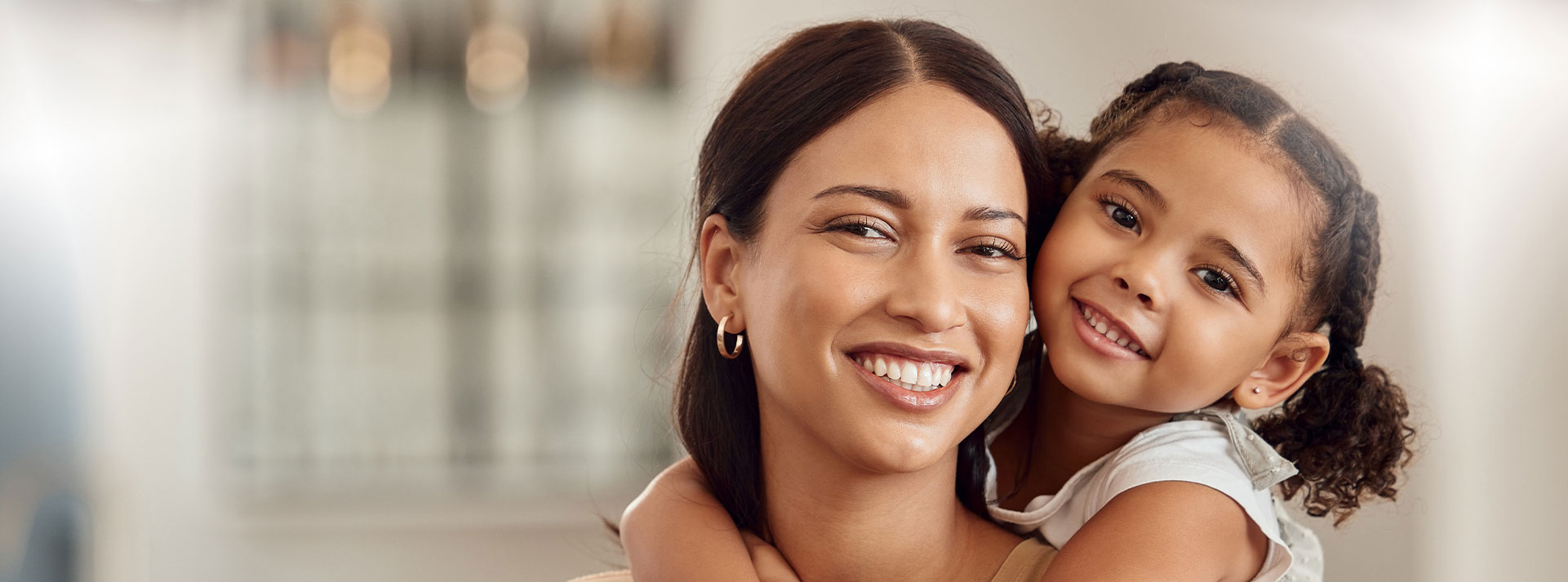 The image shows a woman holding a young child, both smiling, with a blurred background suggesting an indoor setting.