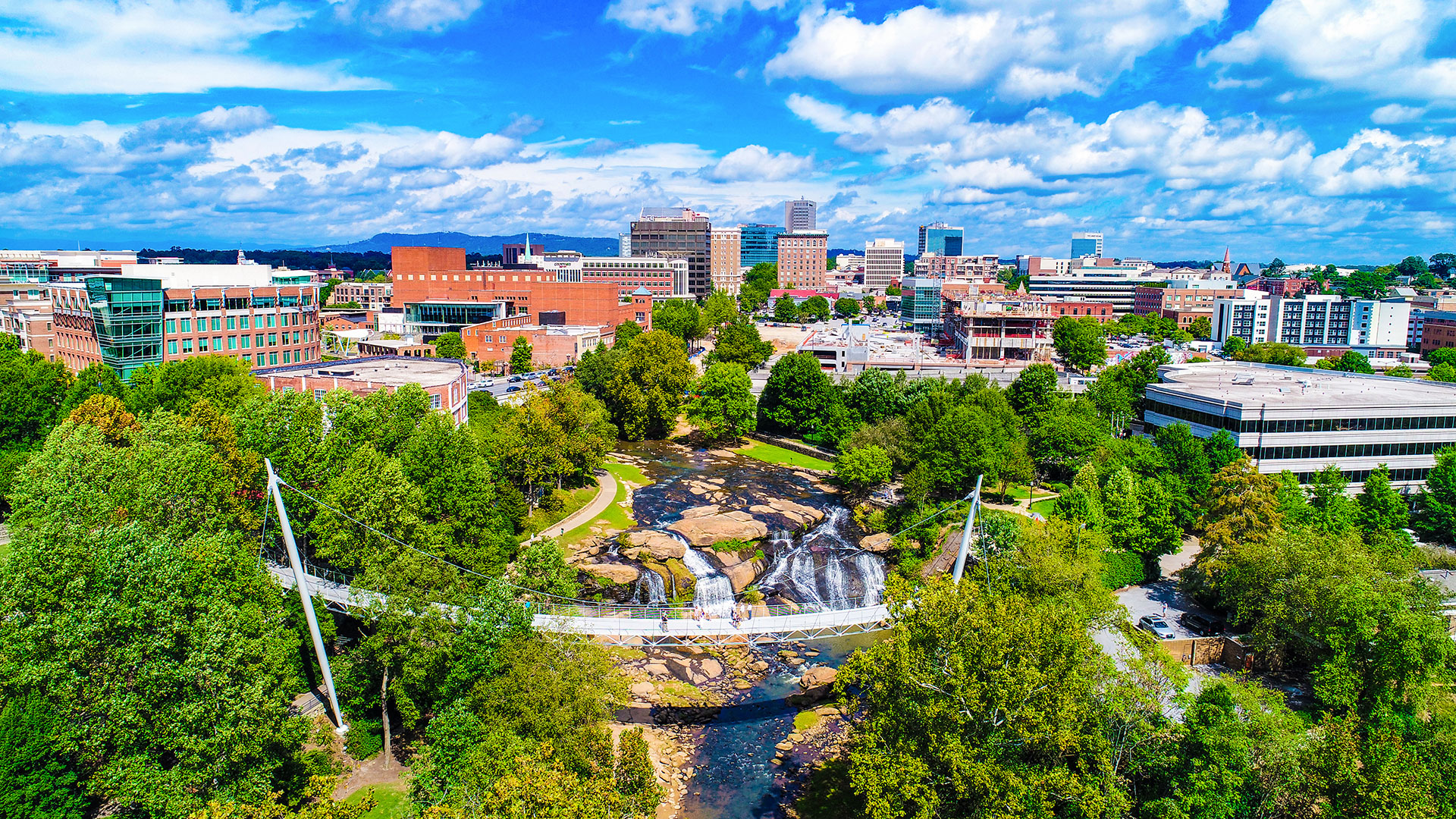 The image shows a scenic view of a cityscape with a prominent waterfall feature and a clear sky above.