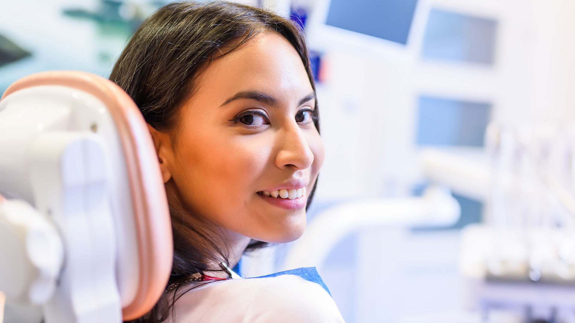 A woman seated in a dental chair, smiling at the camera.