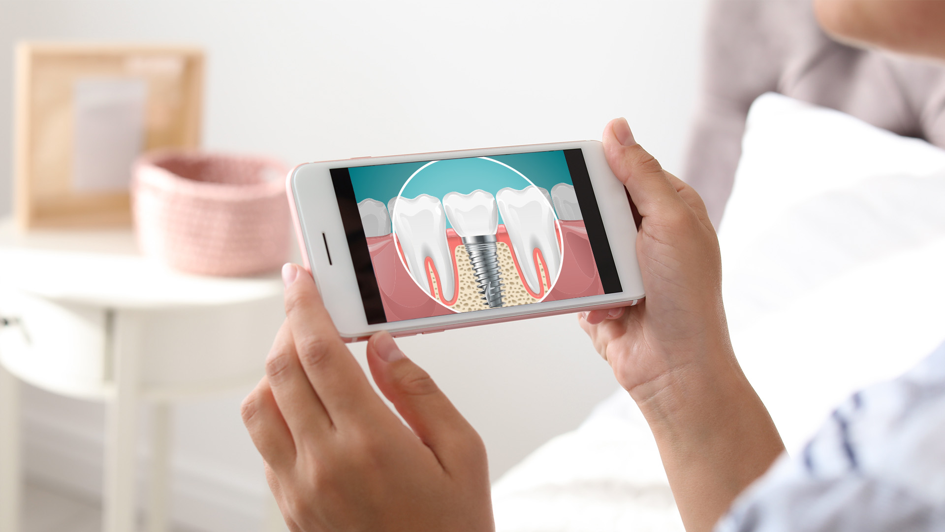 A person holding a smartphone displaying an illustration of a tooth with a dental implant procedure highlighted.