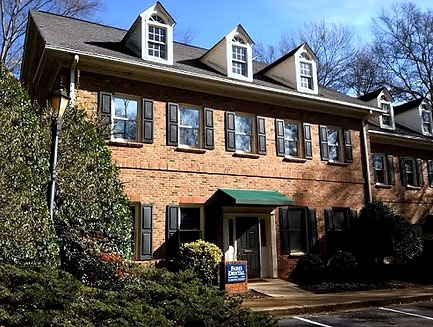 The image shows a two-story building with a brick facade, featuring multiple windows and a covered entrance area.