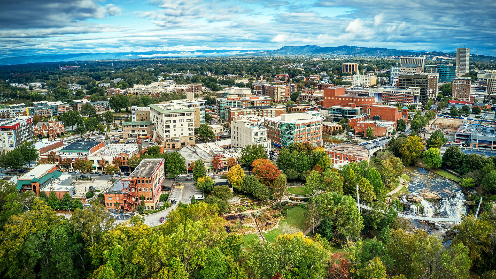 The image depicts an aerial view of a town with various buildings, streets, and green spaces under a partly cloudy sky.