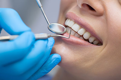 The image shows a person receiving dental care with a dentist using a drill on their teeth while wearing gloves and sitting under a bright light.