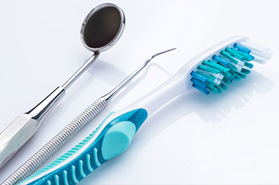 The image displays a collection of dental tools including a toothbrush with blue bristles, a pair of scissors, and other small instruments commonly used in dentistry, all set against a white background.