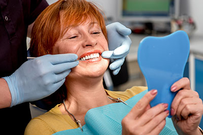 The image shows a woman with red hair sitting in a dental chair, receiving dental care from a professional who appears to be assisting her with a mouthguard or appliance.