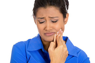 Woman with dark hair, wearing a blue shirt, appears to be in pain or distress while holding her nose.