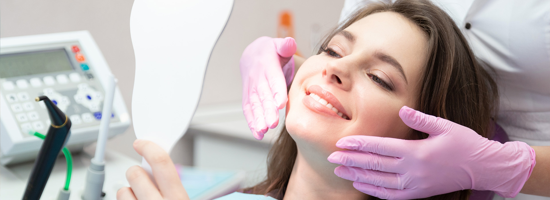 The image shows a woman seated in a dental chair, receiving dental care with an instrument held by a person wearing gloves.