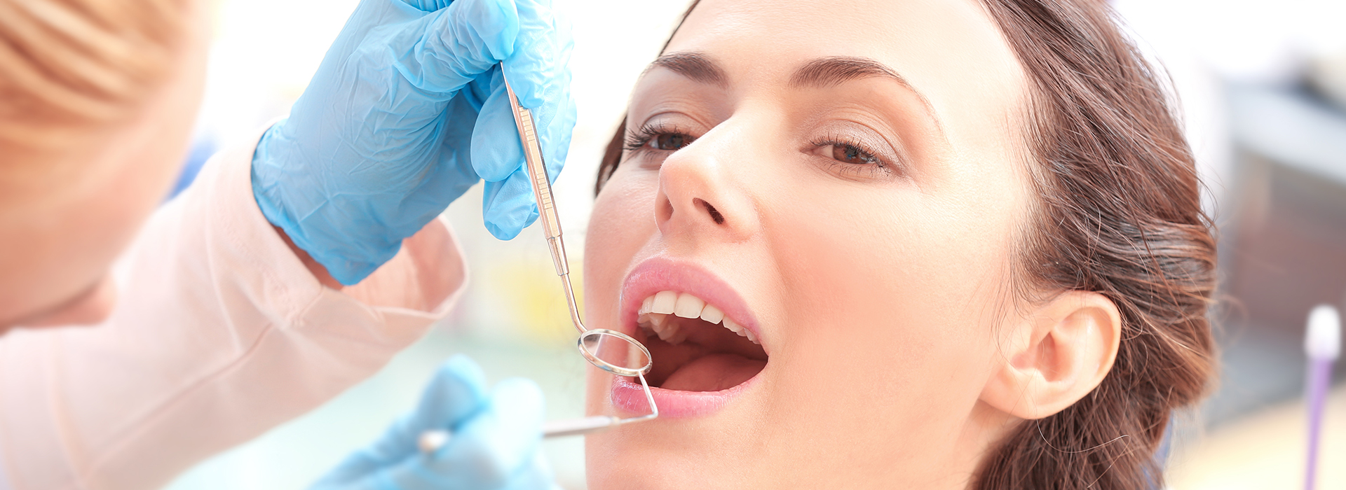 The image shows a person receiving dental care, with a dentist performing a procedure on their teeth using specialized equipment and tools.