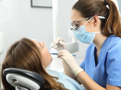 A dental hygienist is performing a cleaning procedure on a patient s teeth while wearing protective gear such as gloves, mask, and eyewear.