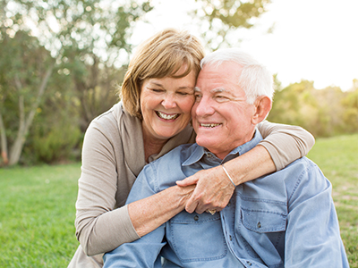 The image shows an elderly couple embracing each other outdoors during the daytime.