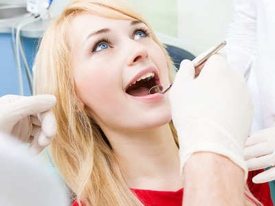 A woman receiving dental care, with her mouth open wide, while a dentist works on her teeth.