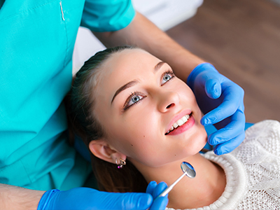 A dental professional performing a cosmetic procedure on a patient s face, with the patient smiling and looking directly at the camera.