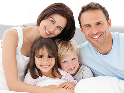 A family of four adults and three children happily posing together on a bed with pillows.