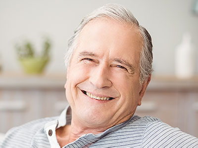 The image shows an elderly man with gray hair, wearing glasses, sitting comfortably in a chair with his eyes closed, smiling slightly, and appears to be enjoying a moment of relaxation.